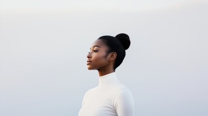 Side profile of a young African woman with her hair in a bun, wearing a white high-neck top against a light background.