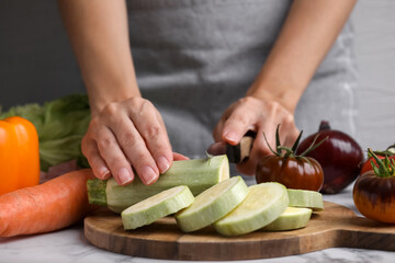 Cooking vegetable stew. Woman cutting zucchini at white marble table, closeup