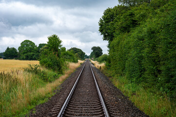 Fototapeta premium Sakskobing, Lolland, Denmark, July 22, 2024 - Straight railroad track through the fields at the Danish countryside