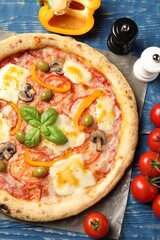Delicious vegetarian pizza and ingredients on blue wooden table, top view