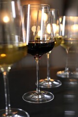 Different tasty wines in glasses on black table against blurred lights, closeup