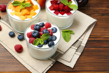 Tasty yogurt with fresh berries, fruits and mint in glasses on wooden table, closeup