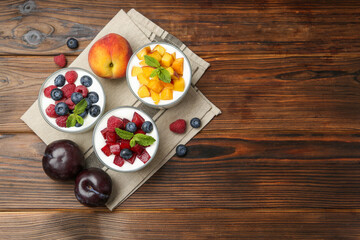 Tasty yogurt with fresh berries, fruits and mint in glasses on wooden table, flat lay. Space for text