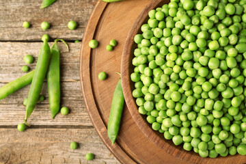 Fresh green peas in bowl and pods on wooden table, flat lay
