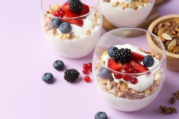 Tasty yogurt with fresh berries and granola in glasses on violet background, closeup