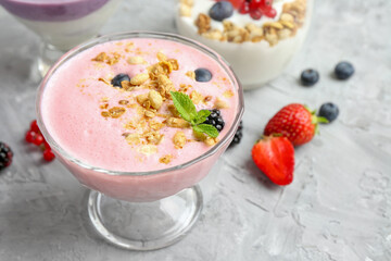 Different tasty yogurts with fresh berries and granola in glass dessert bowls on gray textured table, closeup