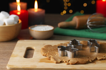 Raw dough, cookie cutters, flour, marshmallows, kitchen tools and burning candles on wooden table