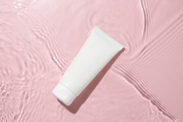 Cosmetic product. Tube with cream in water on pink background, top view