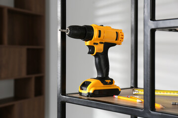 Electric screwdriver, pencils and tape measure on shelving unit indoors