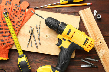 Cordless electric drill, gloves, pencil and construction tools on wooden table, flat lay