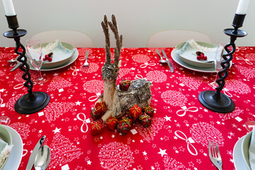 High angle view of table set for Christmas lunch with red tablecloth, wood and tree bark deer...