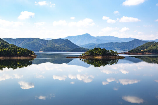 Aerial view of uninhabited island on calm Yongdam Lake with the reflection of cumulus and mountains near Jinan-gun, South Korea 