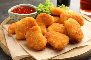 Board with hot chili sauce, lettuce and nuggets on table, closeup