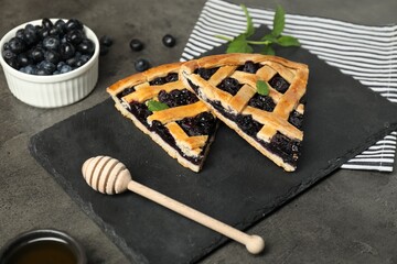 Pieces of tasty homemade pie with blueberries, mint and honey dipper on gray textured table