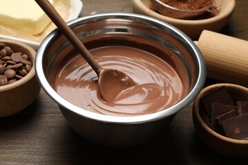 Chocolate dough in bowl and ingredients on wooden table, closeup