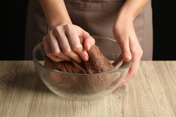 Woman kneading chocolate dough at wooden table, closeup