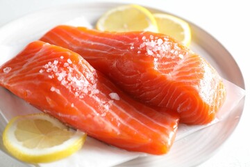 Pieces of fresh salmon with salt and lemon on white table, closeup