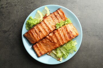 Delicious grilled salmon fillets with lettuce and lemon on grey table, top view