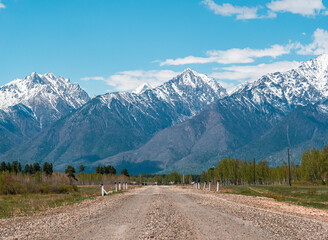 Naklejka premium A winding gravel road leading toward snow-capped mountains