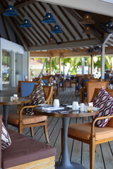 Table on terrace of restaurant or cafe, set with cups, plates, napkins and cutlery. Soft armchairs with cushions. Preparing to receive visitors. Breakfast or lunch in hotel outdoors. Hospitable vibe