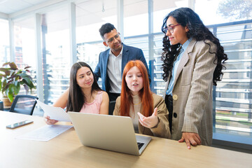Young diverse professional team discussing and developing business strategies around a table at office using laptop