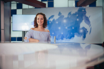  A woman works as a news anchor at a table in front of a camera in a film pavilion