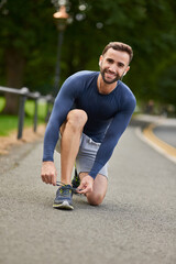 Happy man, portrait and tying shoes with earphones on road for workout preparation or outdoor exercise. Young, male person or runner with smile and getting ready for fitness or training in Italy