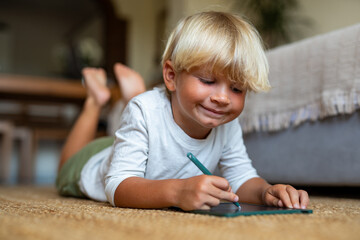 Blonde Boy Lying on the Floor Drawing on a Tablet with a Pen