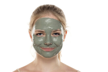 Beautiful young woman posing with a facial green mud mask on her face. Skin care and treatment, spa, natural beauty and cosmetology concept