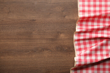 Red checkered picnic tablecloth on wooden table, top view. Space for text