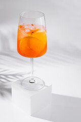 Aperol spritz cocktail standing on white cube casting shadow on white background