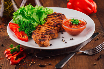 Grilled chicken breast being served with tomato sauce and vegetables on white plate