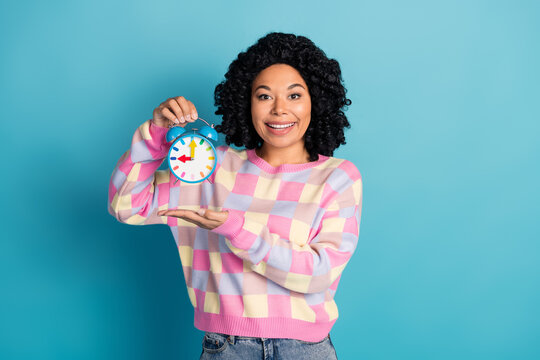 Photo portrait of attractive young woman hold alarm clock dressed stylish pink plaid clothes isolated on blue color background