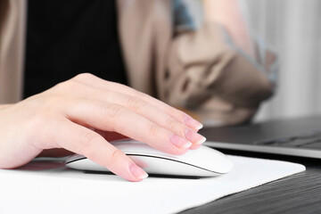 Fototapeta premium Woman using computer mouse while working with laptop at black wooden table, closeup
