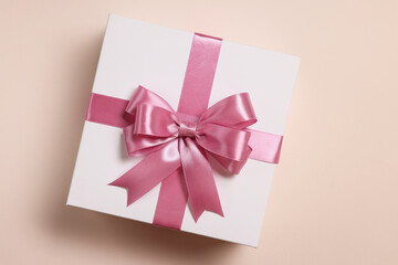 Gift box with bow on beige background, top view