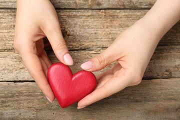 Woman with red decorative heart at wooden table, top view