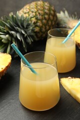 Tasty pineapple juice in glasses and fruits on grey textured table, closeup
