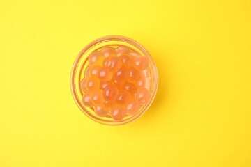 Bright tapioca pearls in bowl on yellow background, top view