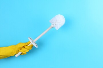 Woman holding white toilet brush on light blue background, closeup. Cleaning tool