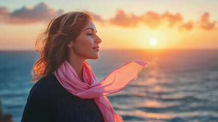 A woman standing on a cliff overlooking the ocean at sunset, with a pink ribbon on her scarf blowing in the wind, symbolizing freedom, hope, and the strength to move forward after a breast cancer