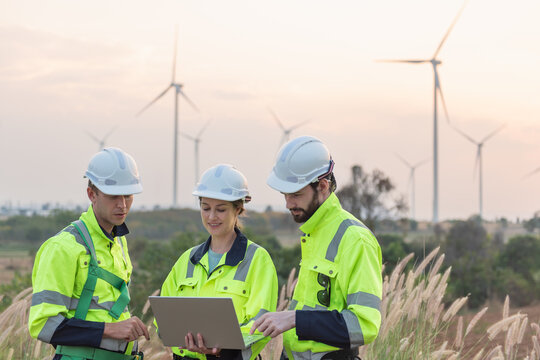 Team of engineers working and using a computer laptop on site in wind turbine farm, Wind turbines generate clean energy source, Eco technology for electric, industry environment