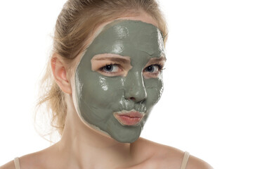 Beautiful young woman posing with a facial green mud mask on her face. Skin care and treatment, spa, natural beauty and cosmetology concept