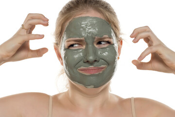 Beautiful nervous woman posing with a facial green mud mask on her face. Skin care and treatment, spa, natural beauty and cosmetology concept