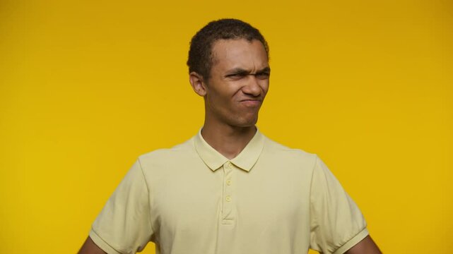 Displeased young man giving double thumbs down yellow background