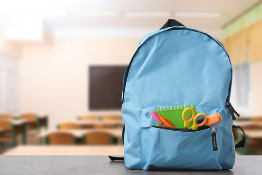 Light blue backpack with stationery on school desk in classroom. Space for text