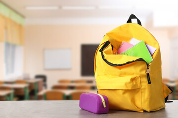 Yellow backpack with stationery on school desk in classroom. Space for text