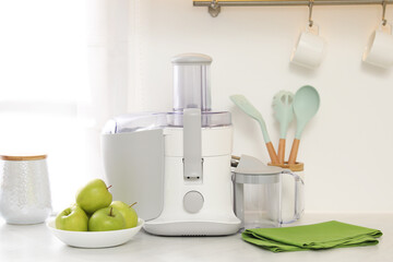 Modern juicer and apples on white counter in kitchen