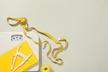 Body fat caliper, measuring tape, scale and notebook on light grey background, flat lay. Space for...