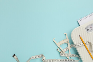 Body fat caliper, measuring tape, scale, pencil and notebook on light blue background, flat lay....