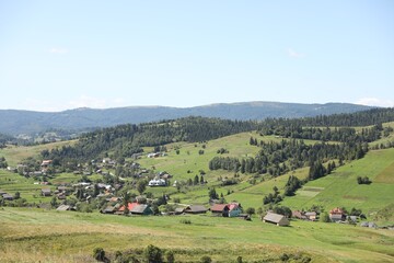 Picturesque view of houses and forest in mountains under blue sky